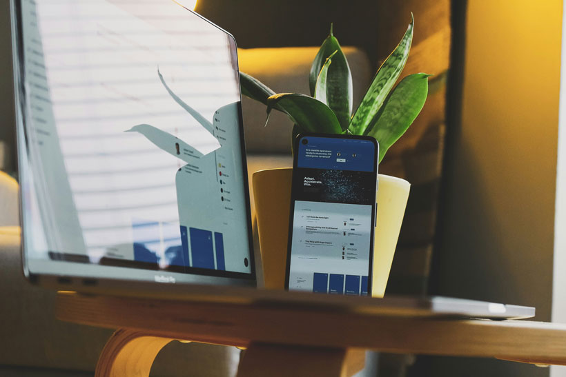 &Eacute;cran d'ordinateur et smartphone affichant un tableau de bord de gestion administrative, pos&eacute;s sur un bureau en bois avec une plante en arri&egrave;re-plan. Ambiance de travail num&eacute;rique et connect&eacute;e
