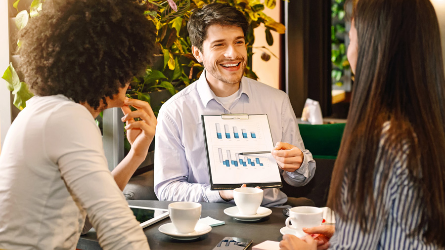 Un expert-comptable pr&eacute;sente une analyse de rentabilit&eacute; &agrave; deux entrepreneuses lors d&rsquo;un rendez-vous professionnel, en expliquant un graphique sur l&rsquo;&eacute;volution des ventes.