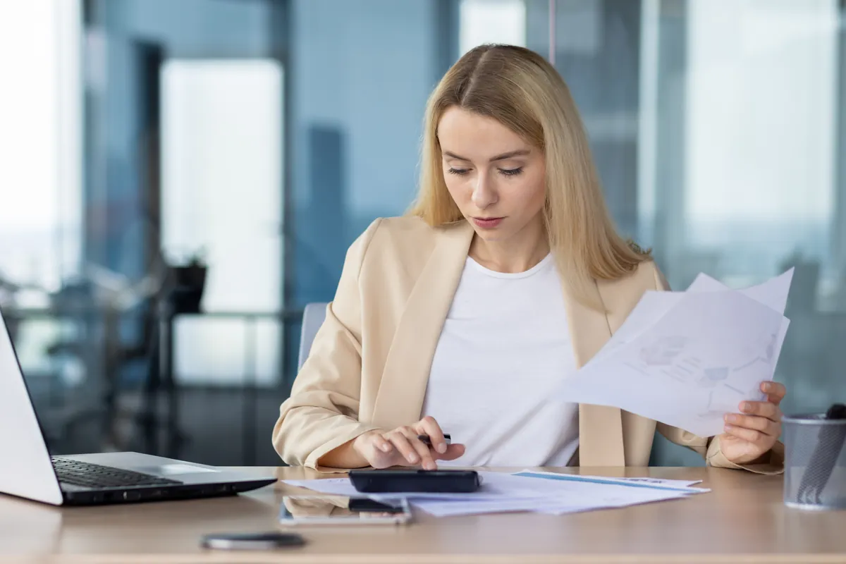 Une professionnelle examine des documents comptables devant un ordinateur portable.